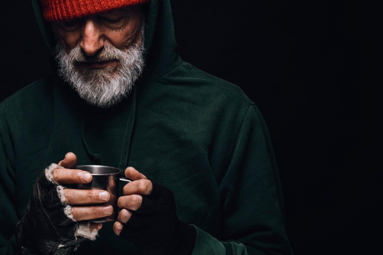 Old homeless man with grey beard covering up in green blanket